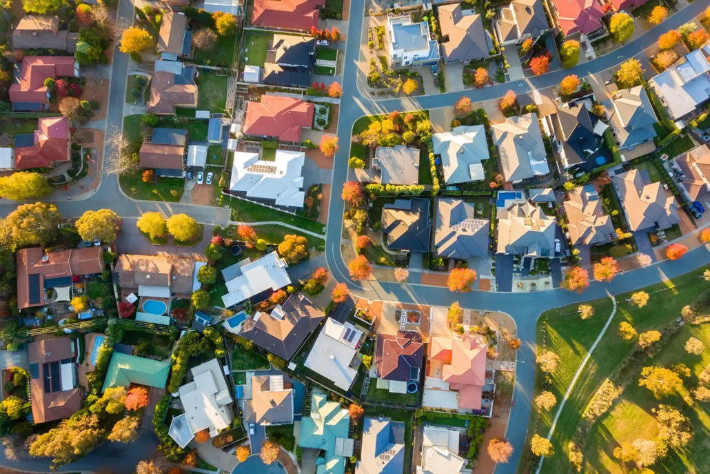 Aerial view of a suburban neighborhood with houses, tree-lined streets, and colorful autumn foliage—perfect for Property Valuations Sunshine Coast. Curving roads and green lawns enhance the scenic appeal throughout the area.