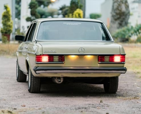 Retro green Mercedes-Benz 230E classic car with illuminated tail lights outdoors.