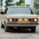 Retro green Mercedes-Benz 230E classic car with illuminated tail lights outdoors.