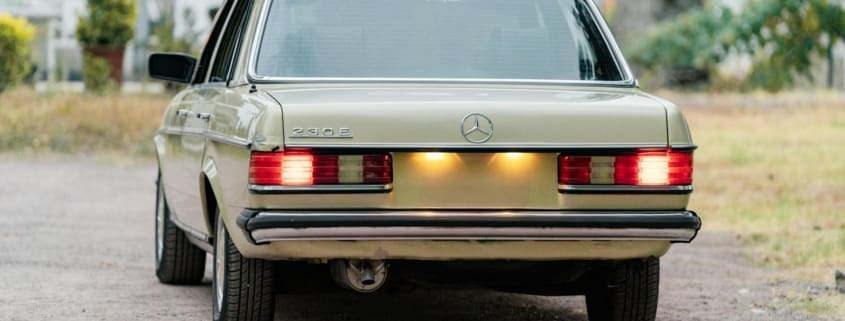 Retro green Mercedes-Benz 230E classic car with illuminated tail lights outdoors.