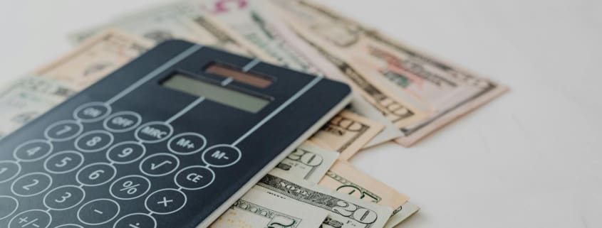 A close-up of a calculator and US dollar banknotes, symbolizing financial calculation and budgeting.