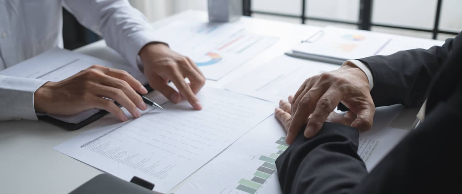 Valuations Rockhampton Valuations Rockhampton, Two people in business attire discuss financial documents with charts and graphs at a desk, pointing at data on printed papers related to Valuations Rockhampton, with notebooks and pens nearby.